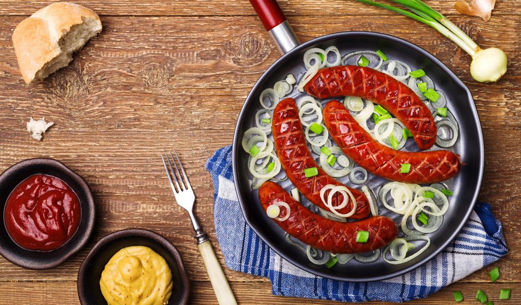 Колбаски барбекю с луком на сковороде на столе с соусом