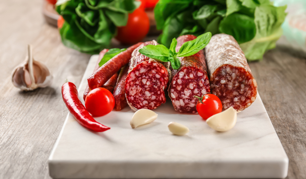 Вкусные колбасные изделия на столе с овощами