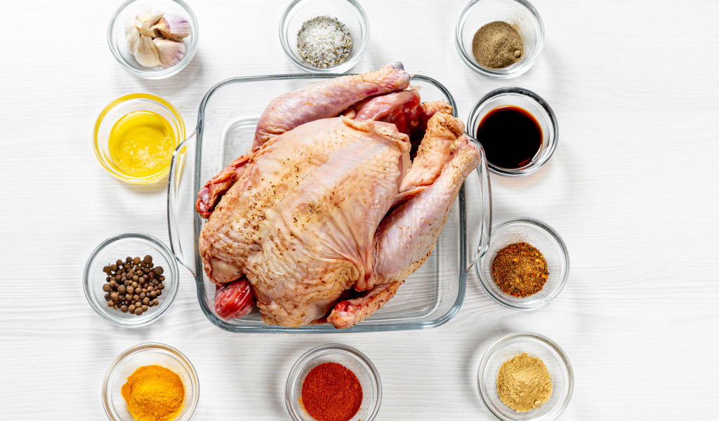 Свежая курица на противне на столе со специями 