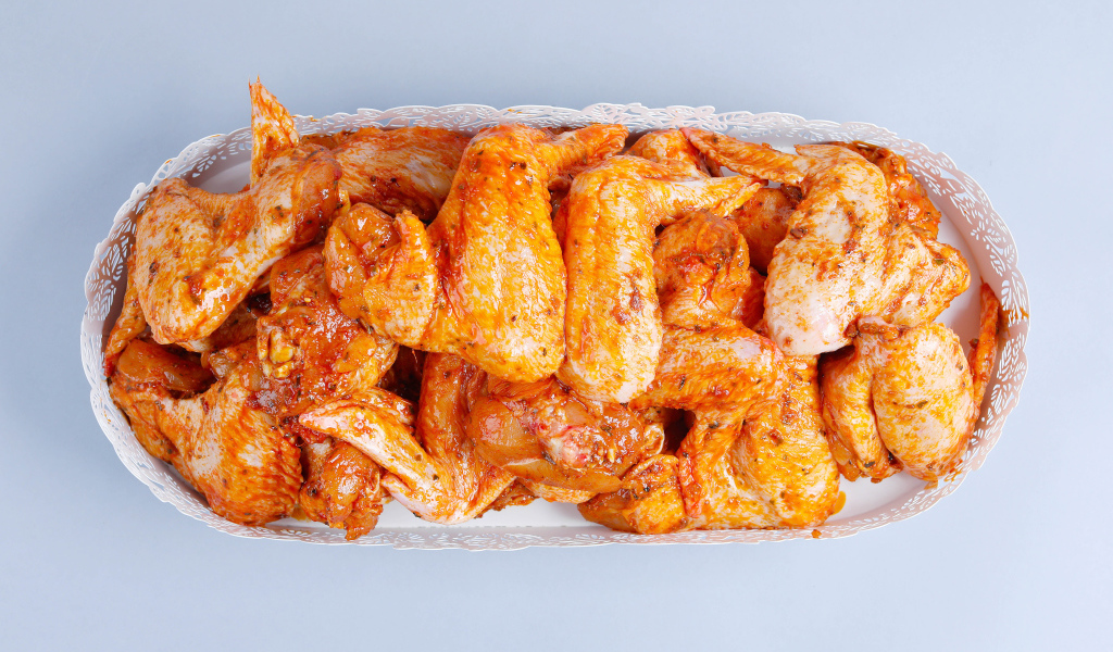 Жареные куриные крылья в белой корзине на сером фоне