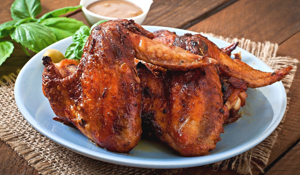 Зажареные куриные крылышки на столе с соусом и базиликом