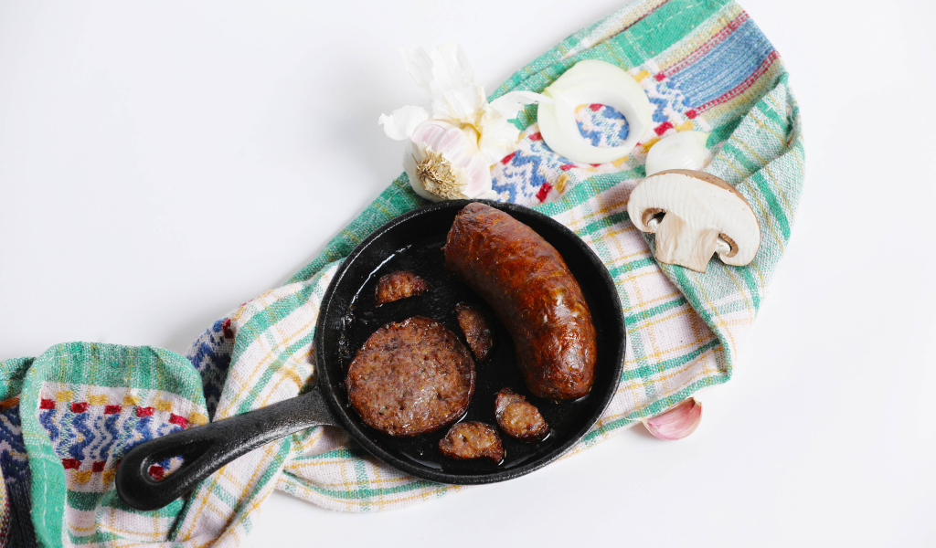 Сковорода с жареной колбасой на столе с полотенцем и чесноком