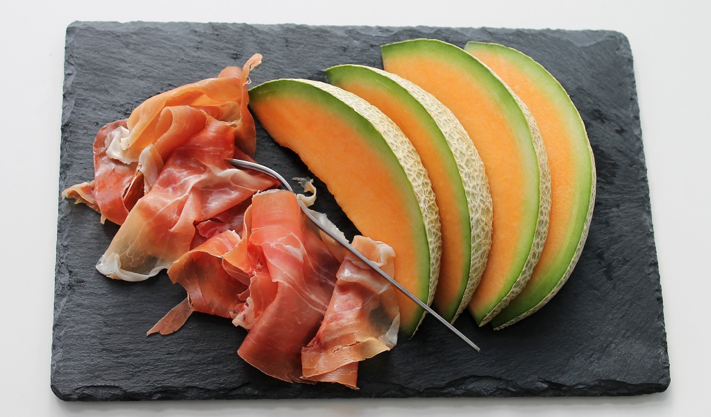 Кусочки дыни на доске с прошутто