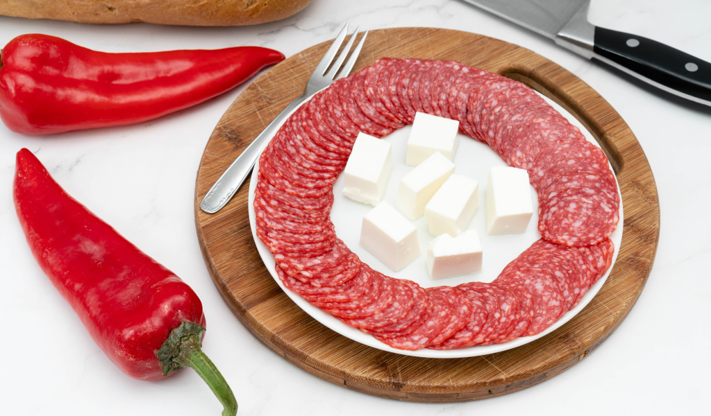 Тарелка с колбасой и сыром на столе с красным перцем