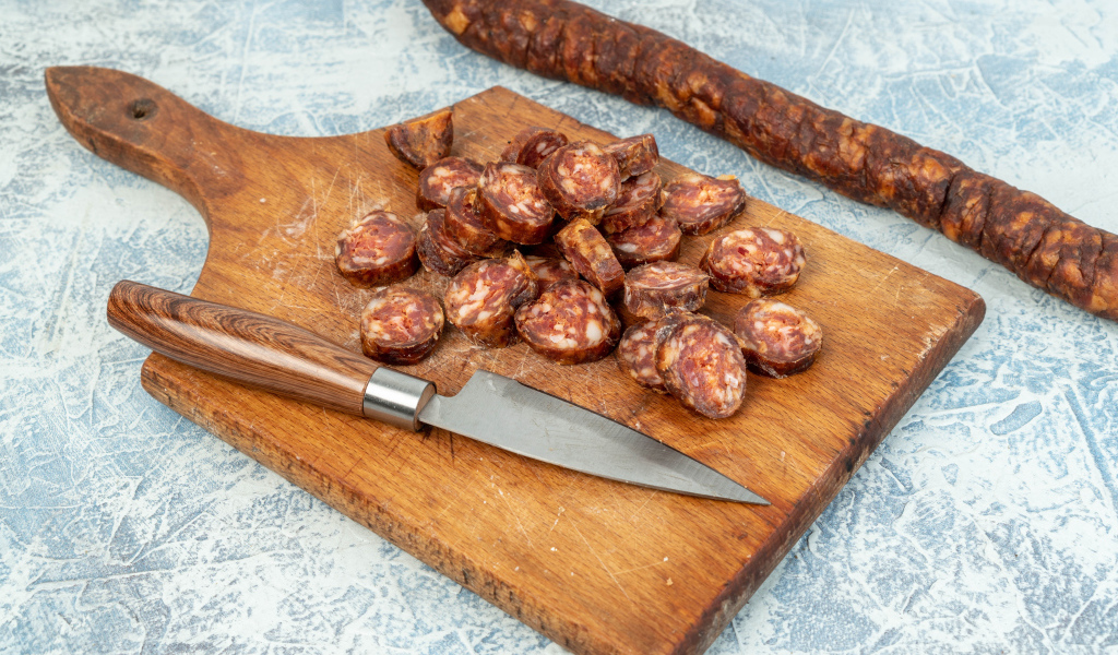 Колбаса нарезана колечками на разделочной доске с ножом 