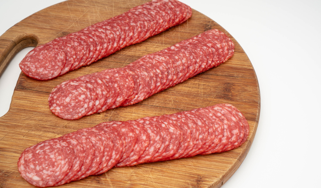 Колбаса тонко нарезана на разделочной доске 