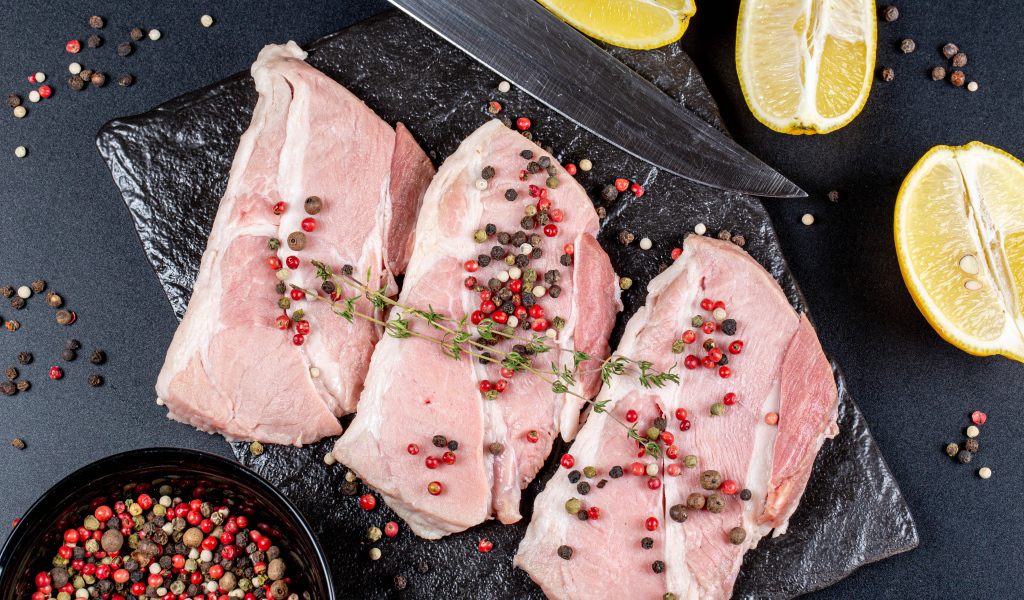 Куски свежего мяса на столе с зернами перца и лимоном