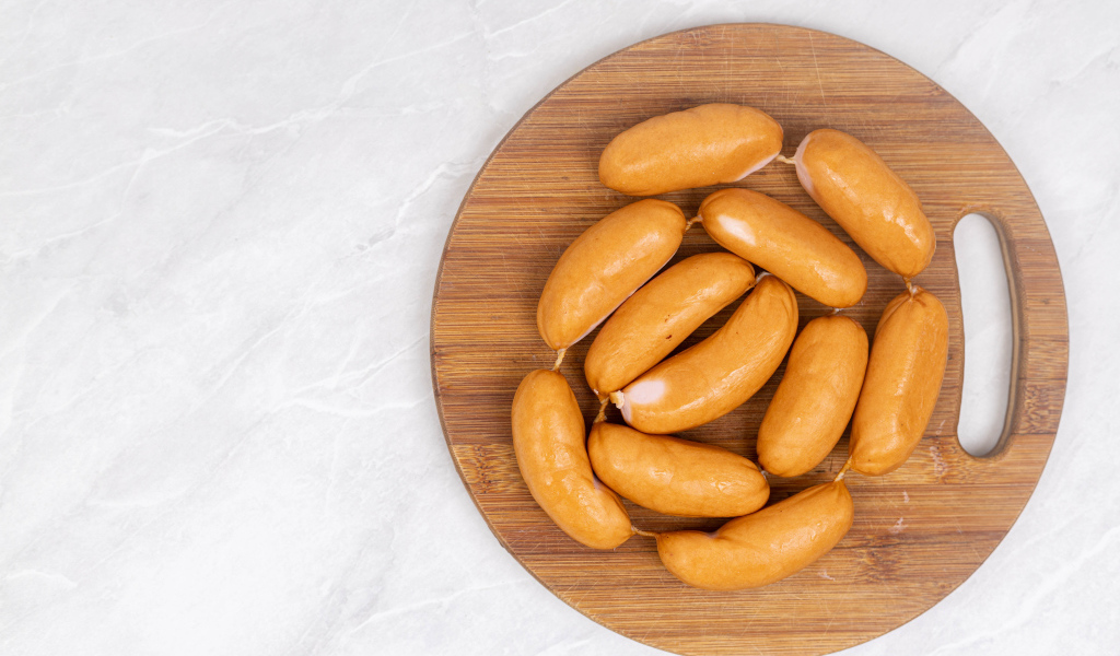 Копченые сардельки на деревянной доске на сером фоне