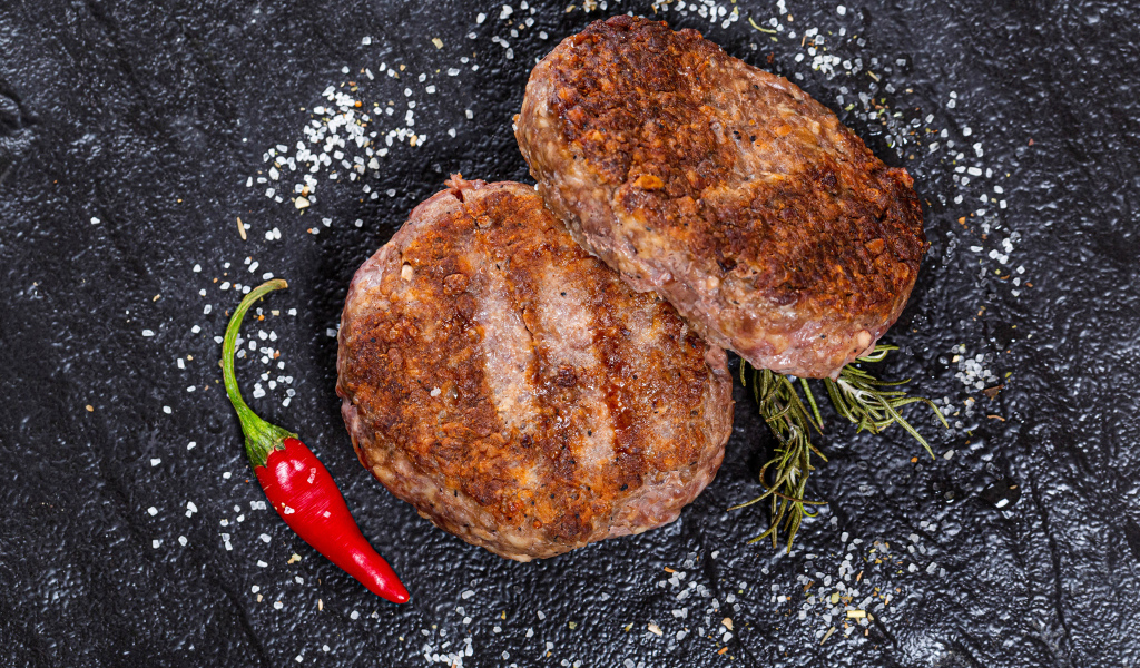 Две котлеты на черной поверхности с красным перцем