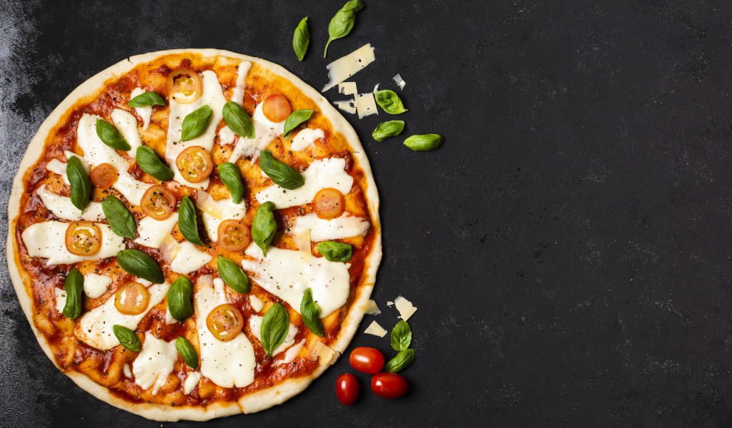 Пицца с сыром, базиликом и помидорами на черном столе 