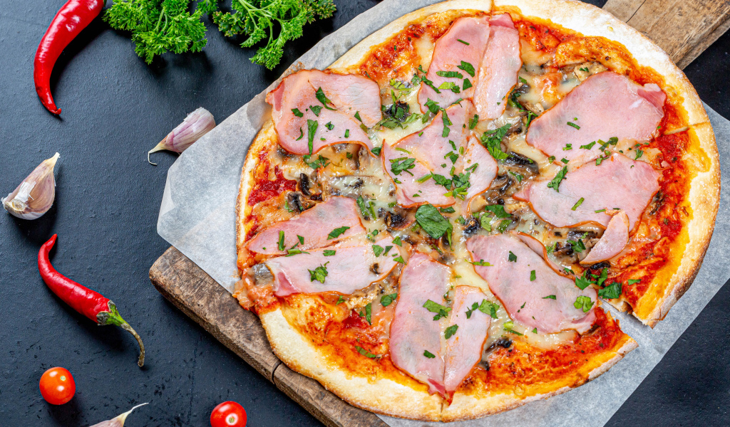 Пицца с ветчиной и грибами на столе с перцем чили, чесноком и петрушкой