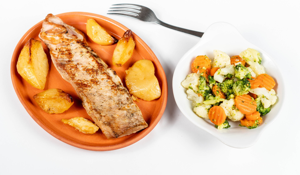 Кусок запеченной рыбы на тарелке с овощами 