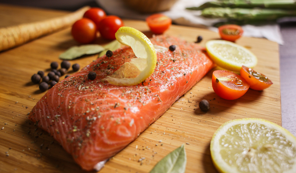 Кусок красной рыбы на доске с лимоном и помидорами