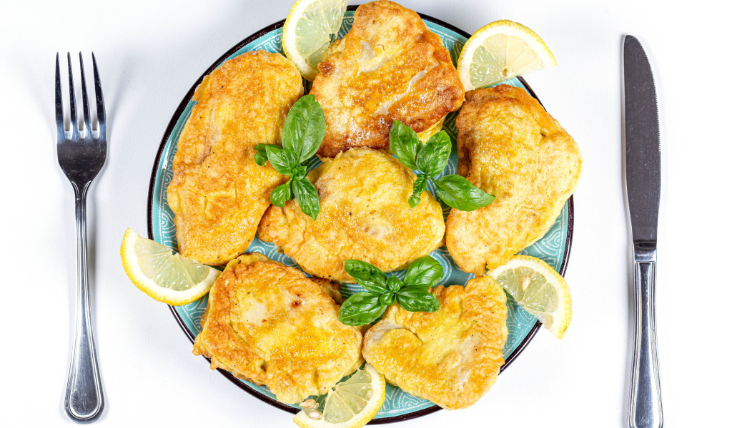 Аппетитная рыба в кляре на тарелке с кусочками лимона и столовыми приборами