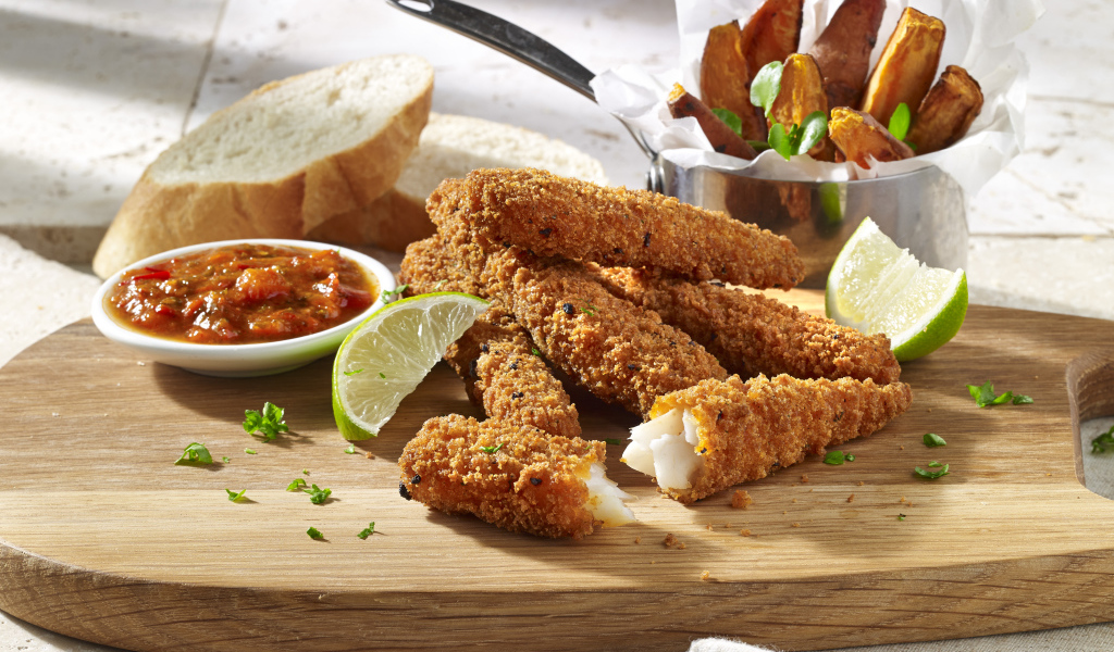 Рыба в панировке на столе с соусом и кусочками лайма