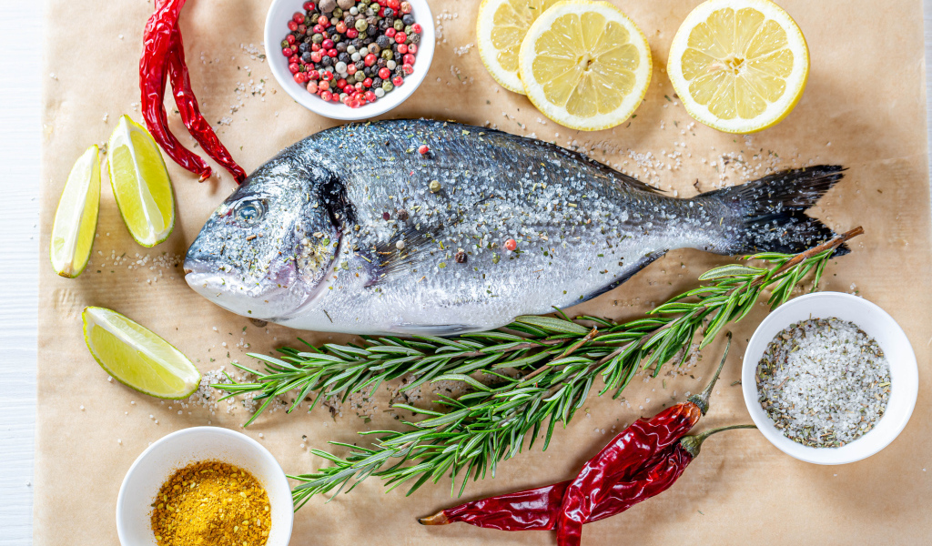 Свежая рыба на столе со специями, лимоном, розмарином и красным перцем
