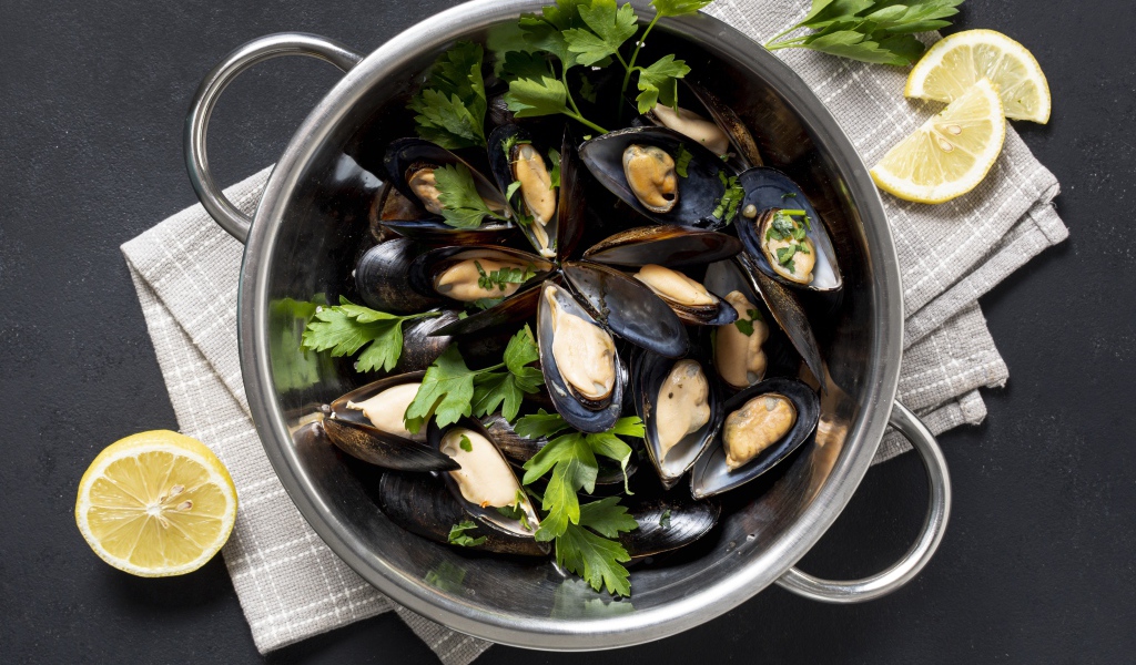 Свежие мидии в кастрюле с зеленью петрушки 