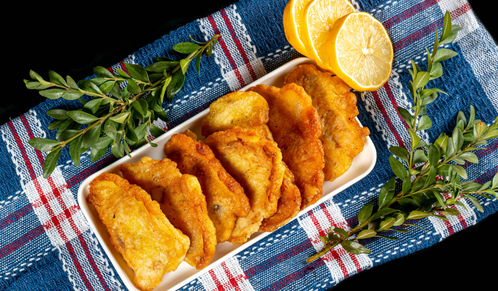 Жареная рыба в кляре на столе с лимоном и зеленью