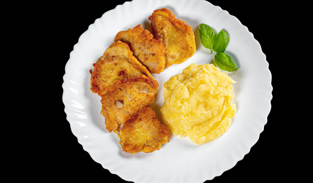 Куски жареной рыбы с картофельным пюре в тарелке на черном фоне