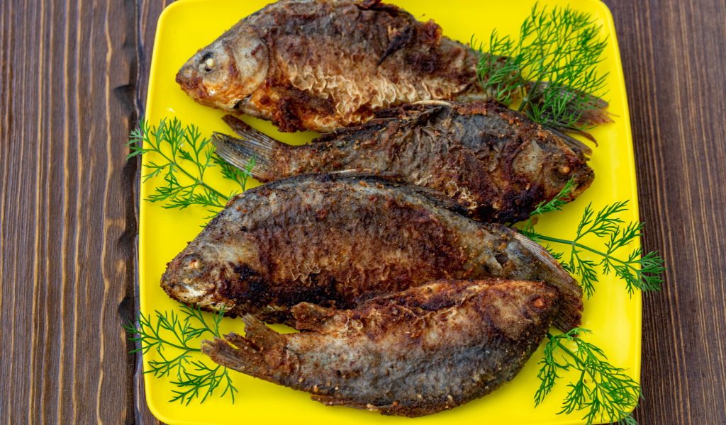 Жареные караси с укропом на желтой тарелке 