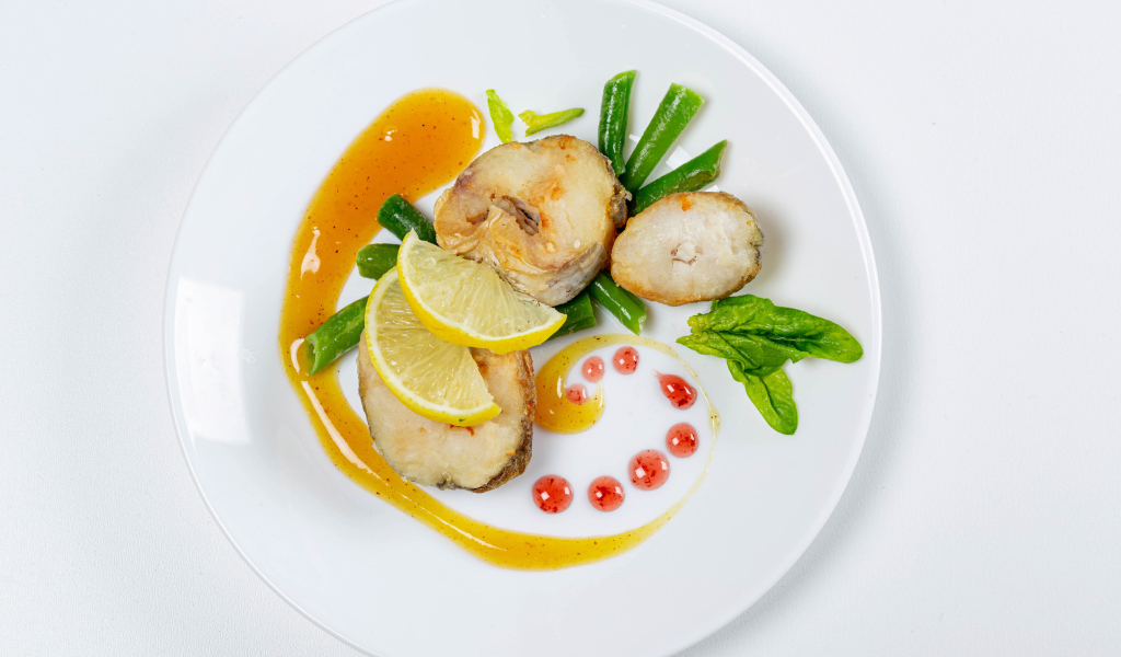 Кусочки жареной рыбы на белой тарелке с лимоном и зеленью