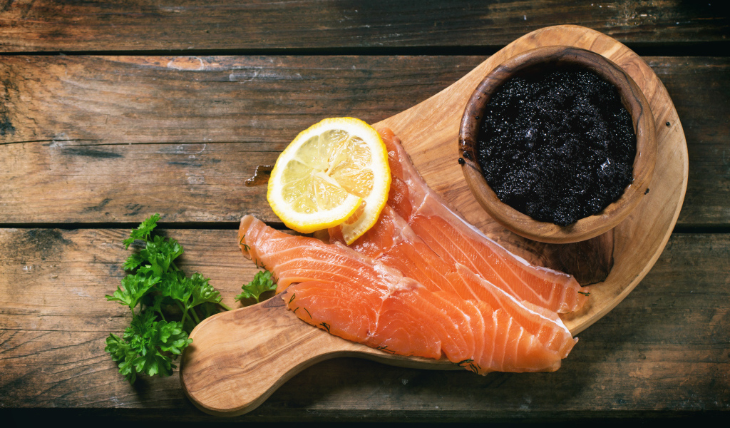 Кусочки красной рыбы с лимоном на столе с черной икрой 