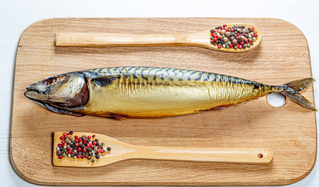 Smoked mackerel on a cutting board with pepper on a white background