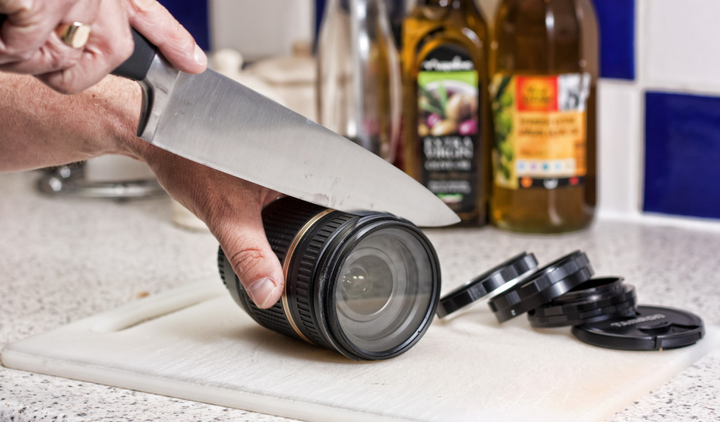 Мужчина нарезает ножом объектив фотоаппарата 