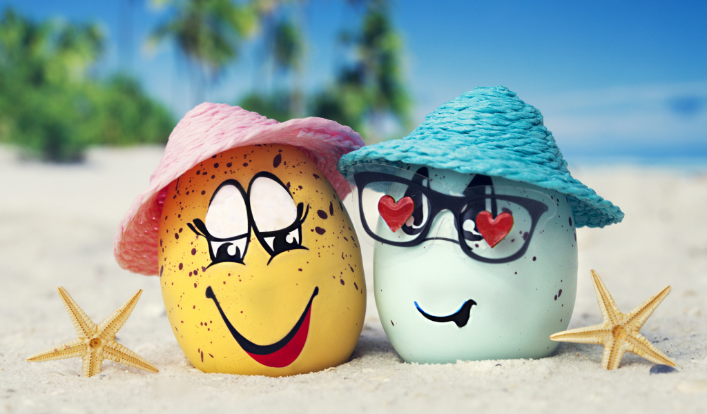 Два яйца в шляпах на песке с морскими звездами летом