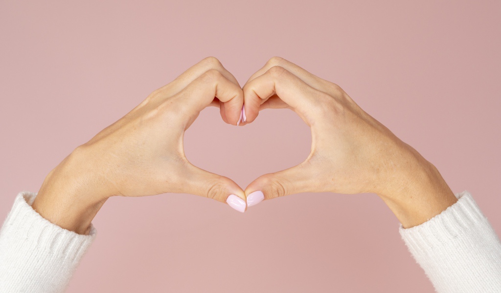 Девушка делает сердце руками на розовом фоне 