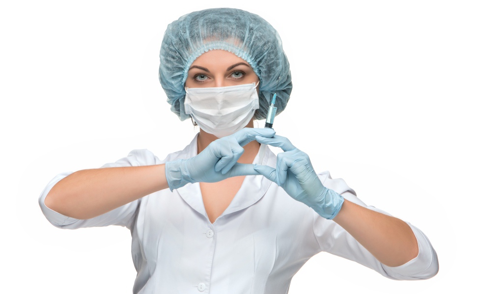 Girl nurse in a mask with a syringe in her hands on a white background