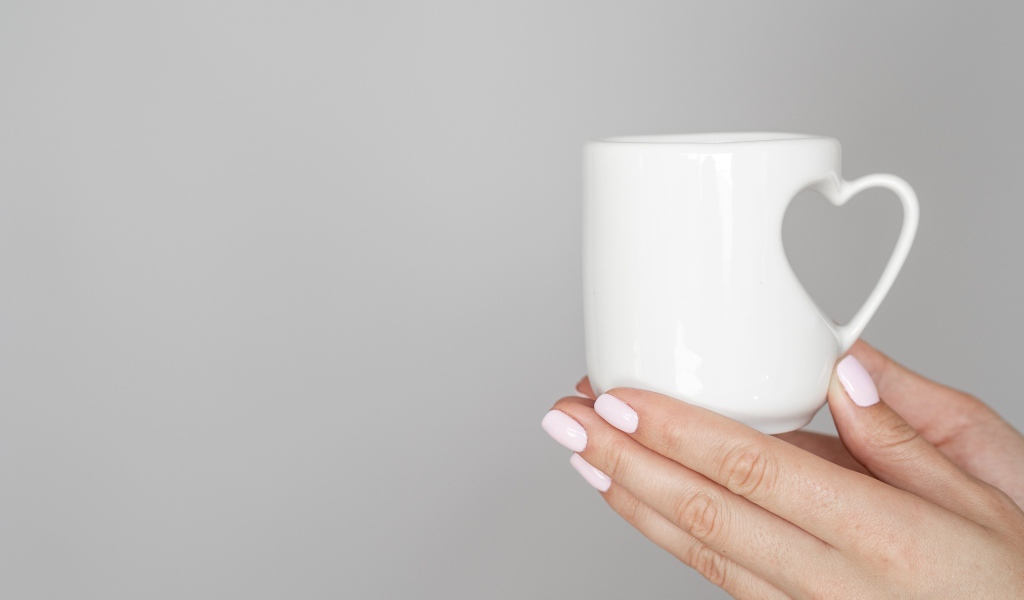 White mug in the hands of a girl on a gray background