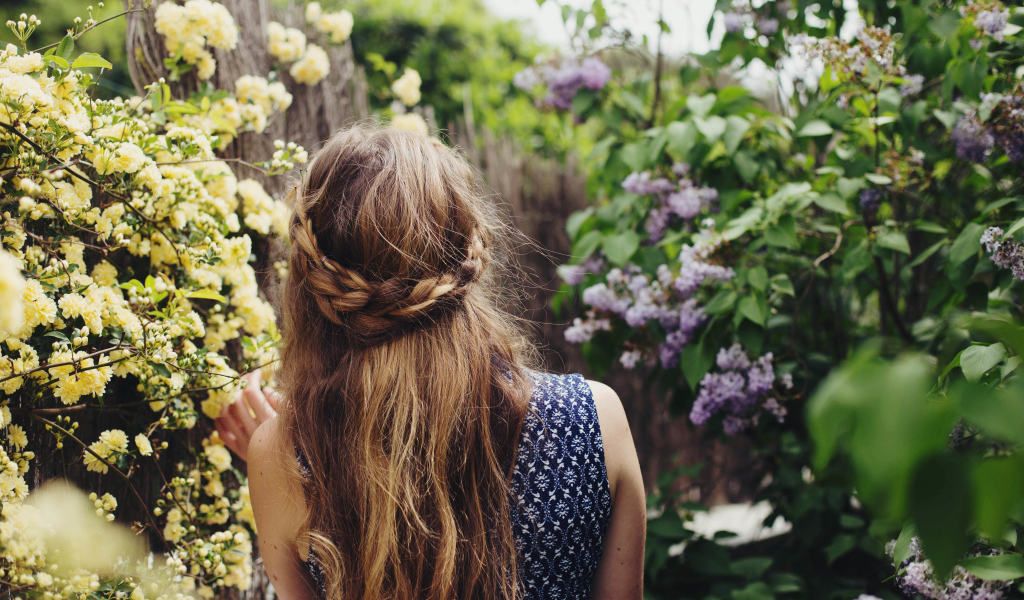 Красивая девушка с косой на голове идет по зарослям сирени 