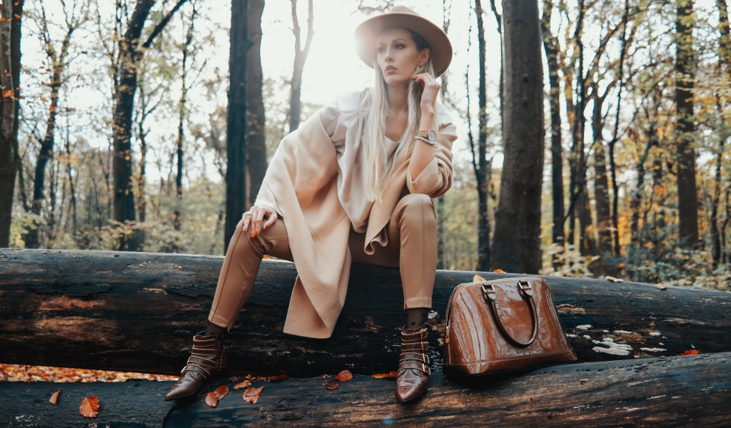 Девушка в пальто сидит на упавшем дереве в лесу 