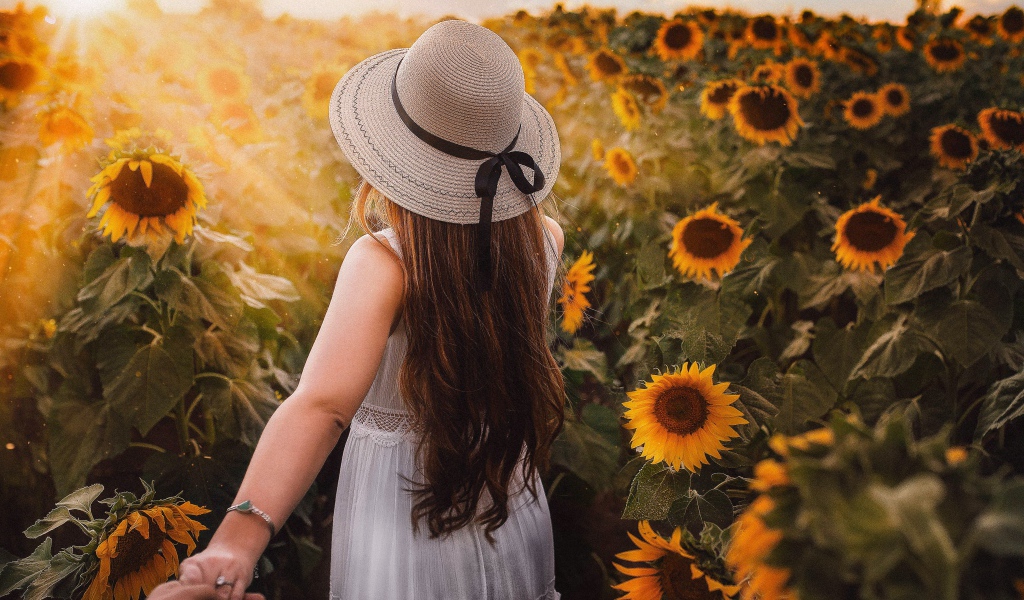 Девушка в белом платье и шляпе гуляет по полю с подсолнухами