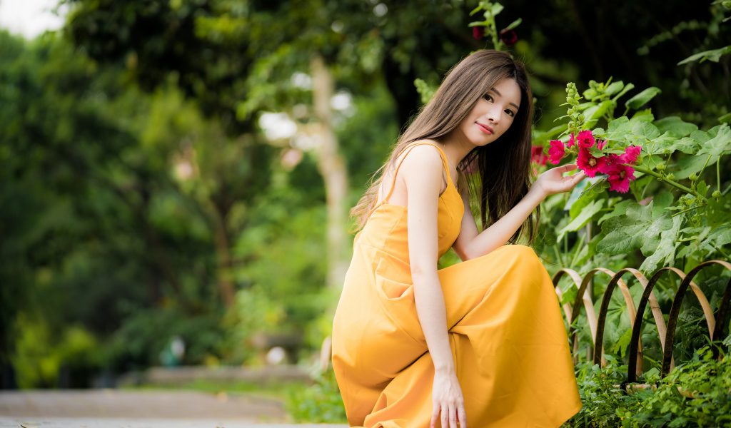 Девушка в желтом платье сидит у цветка мальвы в парке