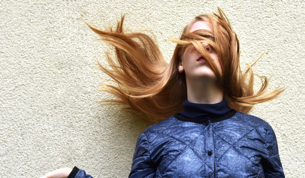 Девушка с волосами на лице стоит у стены