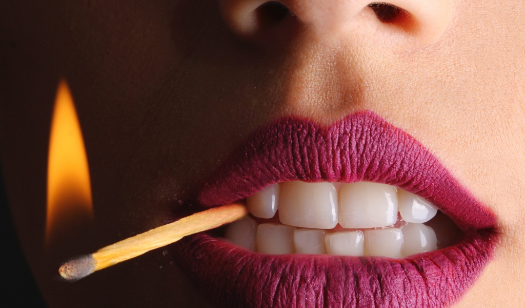 Зажженная спичка в зубах у девушки 