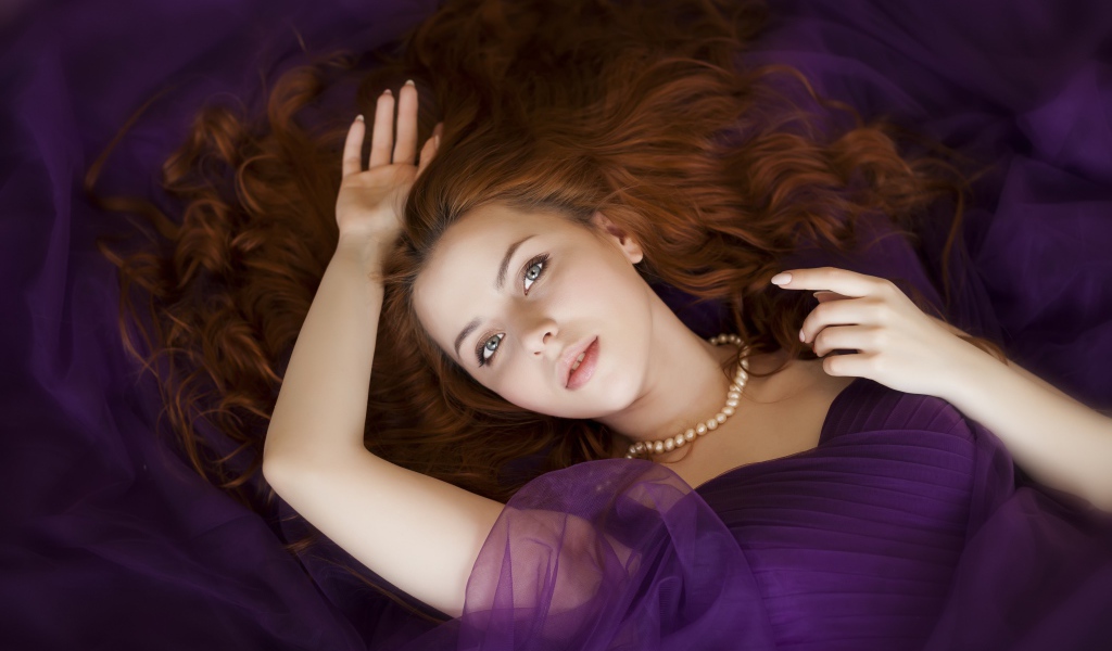 Рыжеволосая девушка в фиолетовом наряде лежит на полу