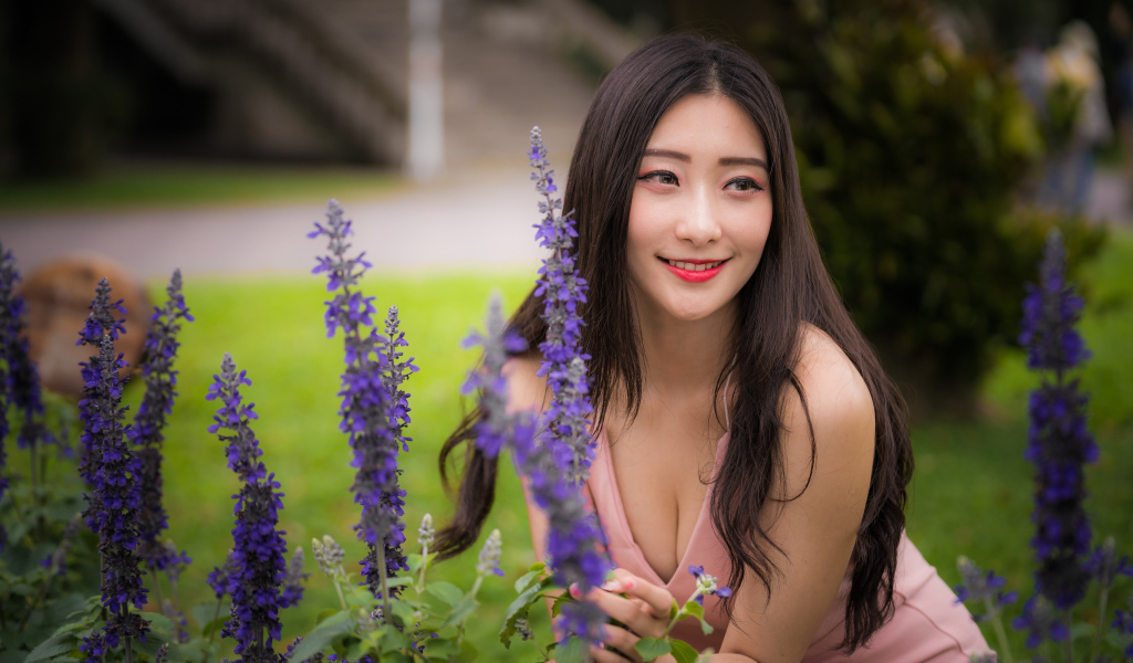 Улыбающаяся азиатка стоит у синих цветов 