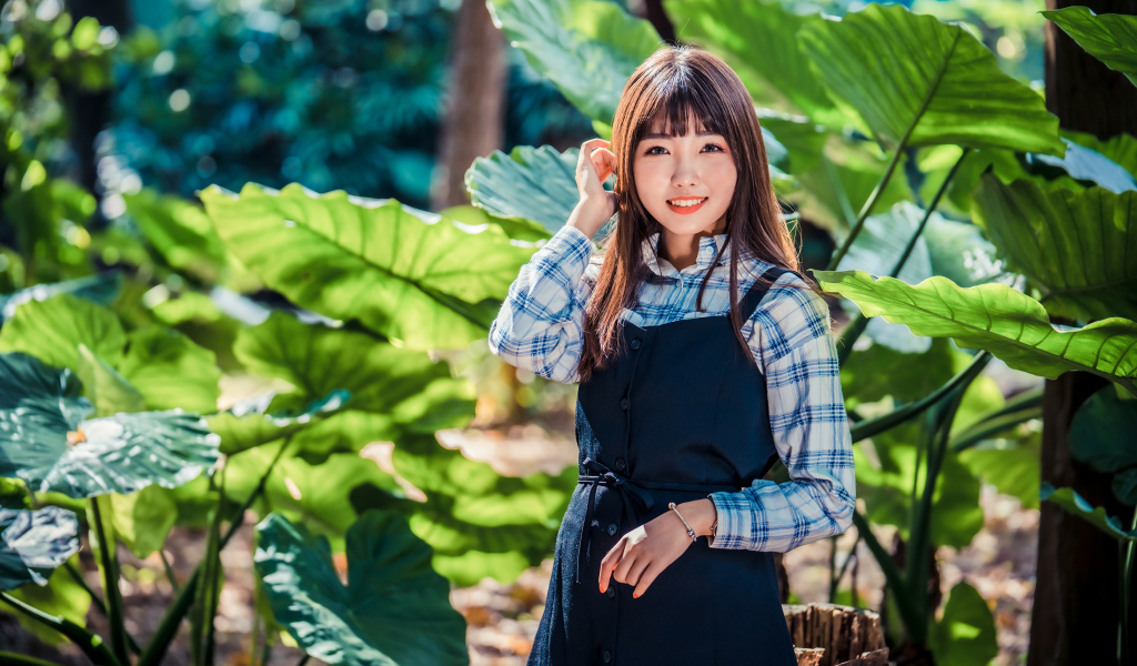 Улыбающаяся девушка азиатка в черном платье стоит в парке