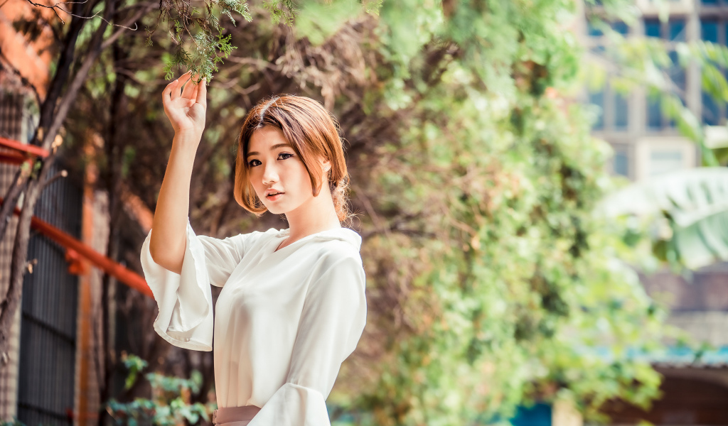 Молодая азиатка в белой блузке стоит у дерева 