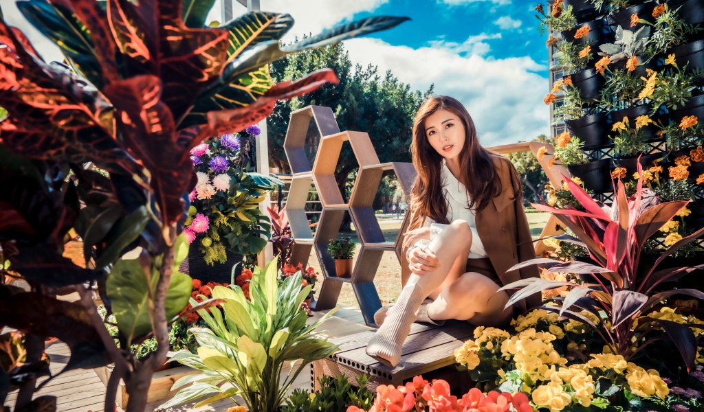 Молодая азиатка сидит возле клумбы с цветами