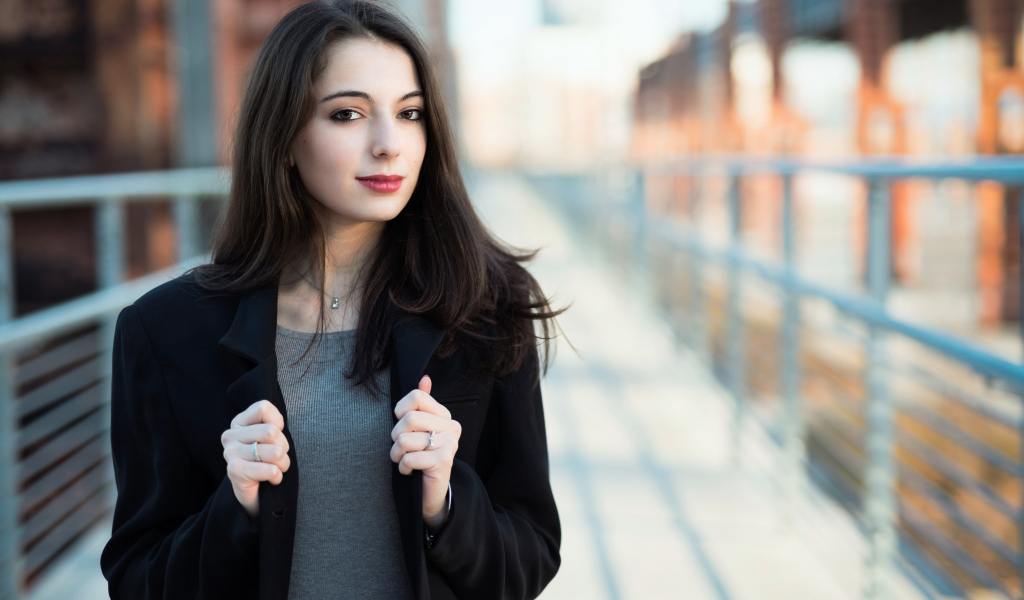 Молодая девушка в черном пальто стоит на мосту