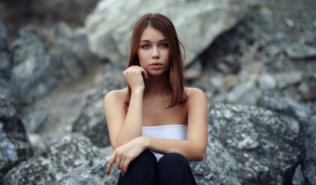 Молодая девушка сидит на камнях 