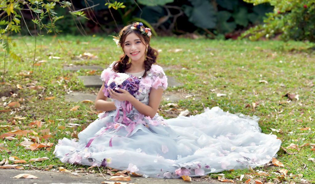 Девушка азиатка в красивом платье сидит на земле с букетом 