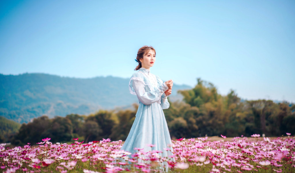 Девушка азиатка в красивом платье идет по полю с цветами космеи