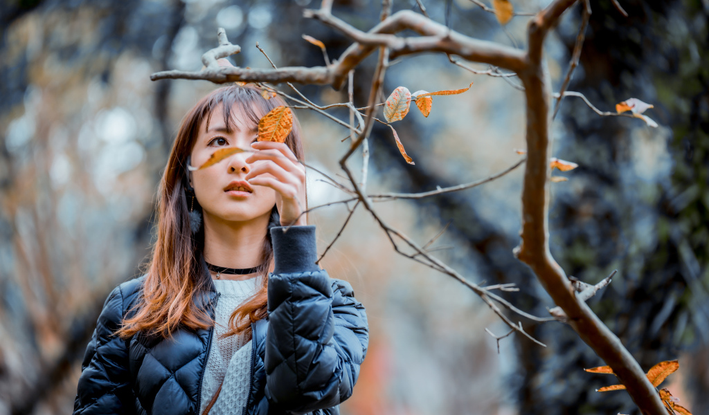 Девушка азиатка в черной куртке у дерева