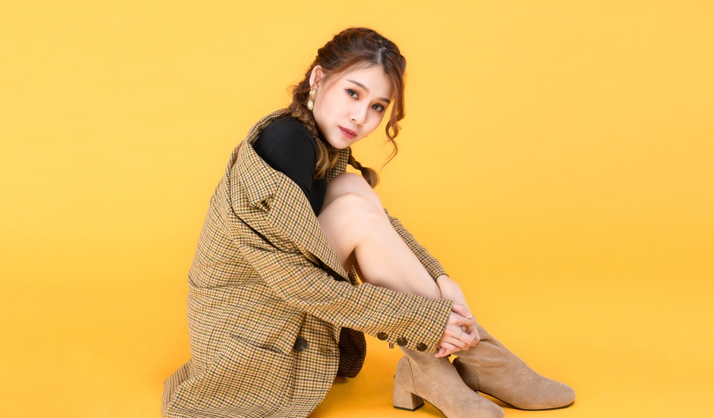 Девушка азиатка в пальто на желтом фоне 