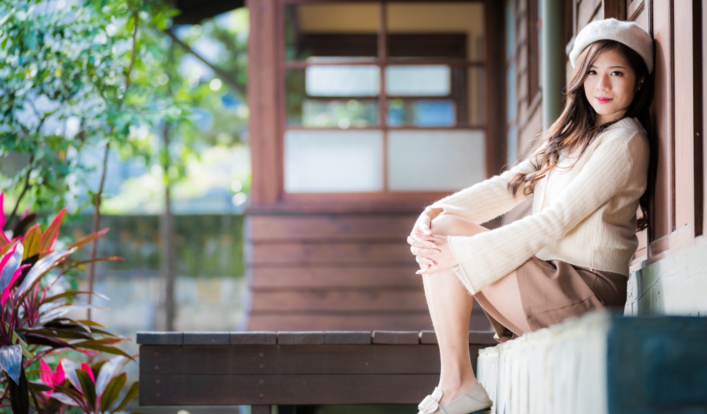 Девушка азиатка в свитере сидит на пороге 